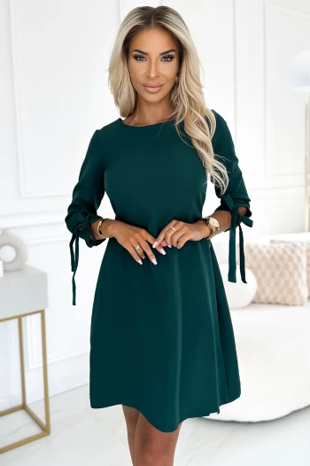 The woman in the photo is wearing a stunning emerald evening gown, highlighting its elegant drape and rich color. The model showcases the evening dress with a chic clutch, emphasizing its sophisticated style.