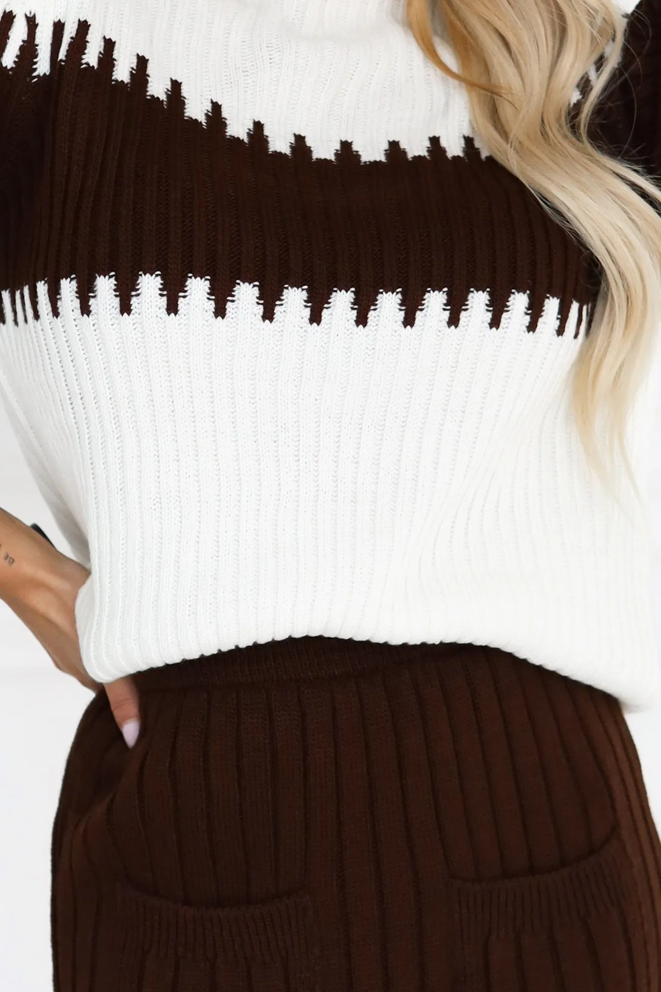 The woman in the photo is wearing a stylish ribbed knit sweater with a striking contrast pattern. The brown and white long-sleeve sweater adds a cozy and fashionable touch to any outfit.