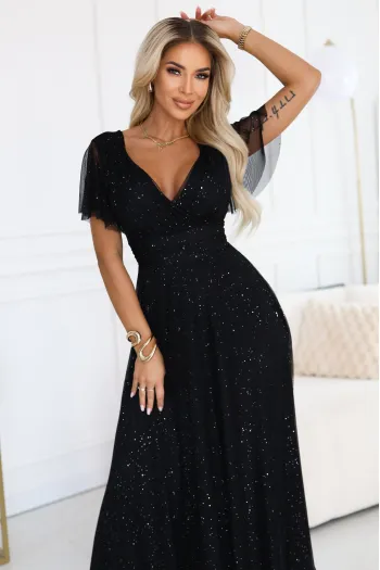 The woman in the photo is wearing a shimmering black evening gown adorned with subtle sparkles. The evening gown drapes elegantly, showcasing a V-neck design and flowing sleeves.