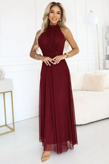 The woman in the photo is wearing a flowing red halter neck gown that drapes elegantly to the floor, perfect for formal occasions. This red gown features delicate detailing around the waist, adding a touch of sophistication and style.
